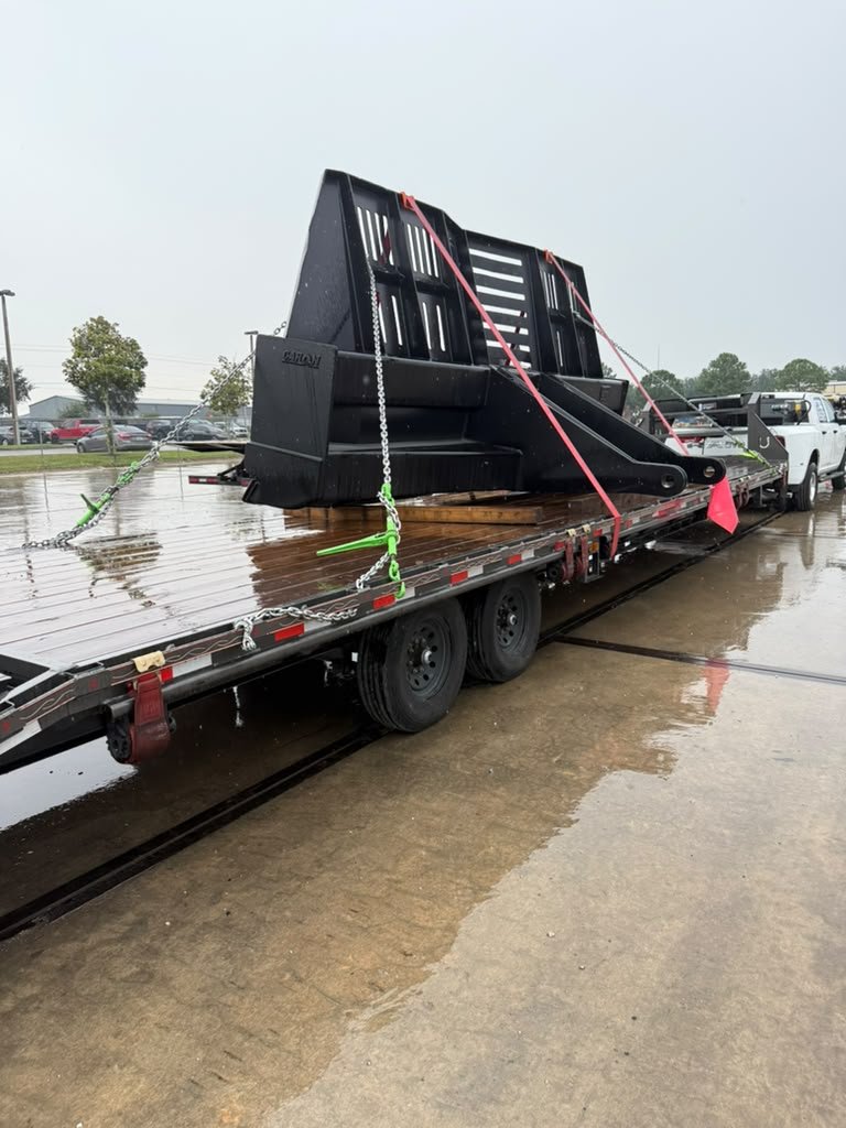 Tráiler hotshot de dos ejes con estructura metálica industrial asegurada con cadenas y correas, remolcado por una pickup blanca.