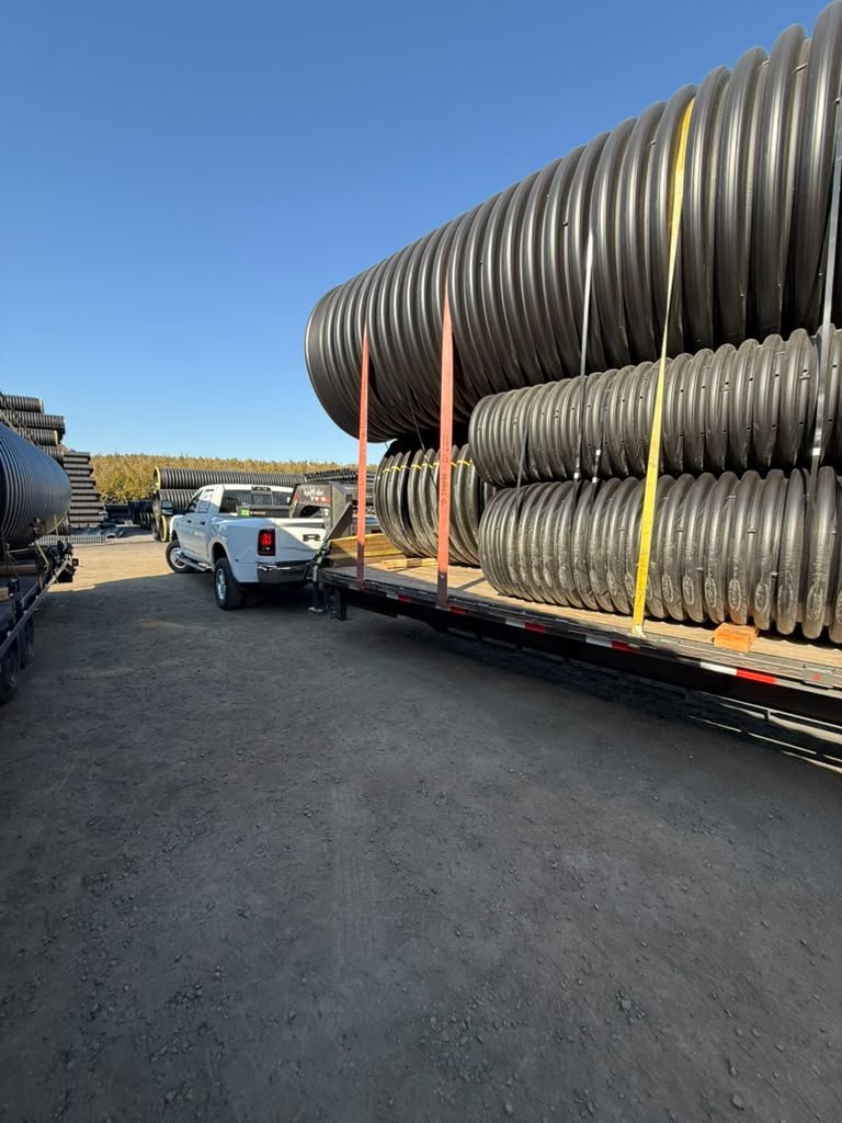 Pickup blanca con tráiler de plataforma cargado con tuberías de gran diámetro para transporte hotshot.